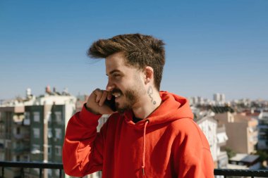 Telefon görüşmesi, kırmızı tişörtlü genç adam balkonda telefonla konuşuyor, telefonla iletişim kuran yakışıklı bir arkadaş.