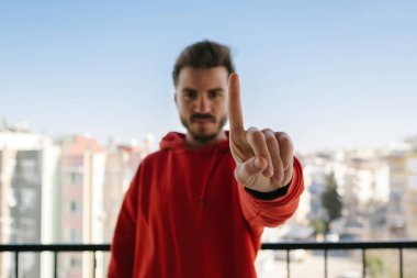 Kırmızı kapüşonlu genç adam parmağını kaldırdı ve kızgın bir ifade takındı. Hiç hareket göstermedi. Eline odaklan..