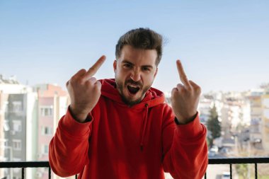 Young handsome man wearing red hoodie showing middle finger doing fuck you bad expression, provocation and rude attitude. Screaming excited.