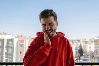 Kötü diş ağrısından muzdarip kırmızı kapüşonlu genç yakışıklı bir adam, boş bir alan. Diş sorunları konsepti.