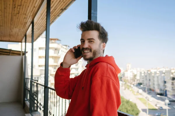 Gülümseyen, kırmızı kapüşonlu genç adam akıllı telefonla konuşurken metal çitlere eğilip kameraya büyük bir gülümsemeyle bakıyor. Kız arkadaşınla konuş..