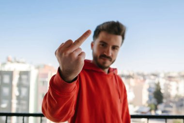 Orta parmak, genç adam hiçbir şeyi umursamaz ve kameraya, ilgisizliğe ve dinlenmeye el sallar.