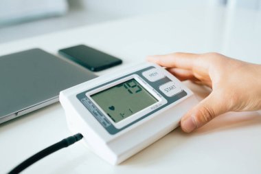 Evde elinde tıbbi elektronik cihazla kan basıncını dijital tonometreyle ölçen genç adam kontrol ediyor..