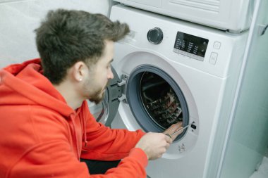 Banyoda çamaşır makinesini tamir eden kırmızı kapüşonlu genç adam..