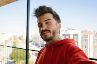 Poz veren, selfie çeken genç bir adam, kırmızı kazak giymiş sakallı yetişkin bir erkek.