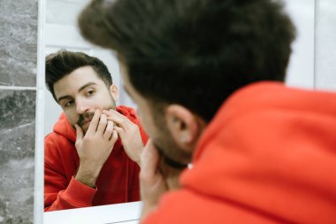 Sivilce, genç bir yetişkin aynanın önünde sivilce çıkarmaya çalışıyor, insan yüz sağlığından memnun değil, yüz ürünleri ve serumları denemeli.