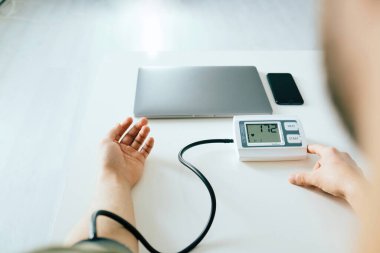 Evdeki kan basıncını ölçen genç adamın omuzlarının üstünden. Modern tonometre kullanmak, stresten kaynaklanan hipertansiyonu tecrübe etmek..