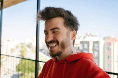 Kırmızı kapüşonlu genç adam şehrin arka planında gülüyor..