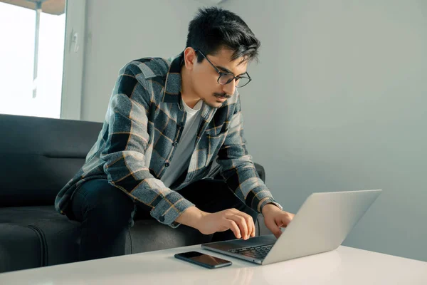 Evdeki kanepede oturan gömlekli genç adam internette çalışıyor, gülümsüyor, mutlu ruh hali, serbest çalışan, serbest zaman geçiren, rahat, modern iş hayatı tarzını kullanıyor.