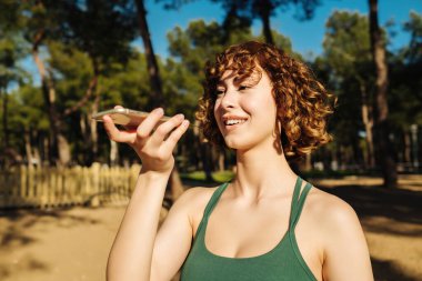 Cep telefonu ya da dijital yardım uygulaması kullanarak telefonu tutan mutlu genç kızıl saçlı kadın sanal asistanı, kayıt mesajını ya da akıllı telefondan konuşmayı etkinleştir.