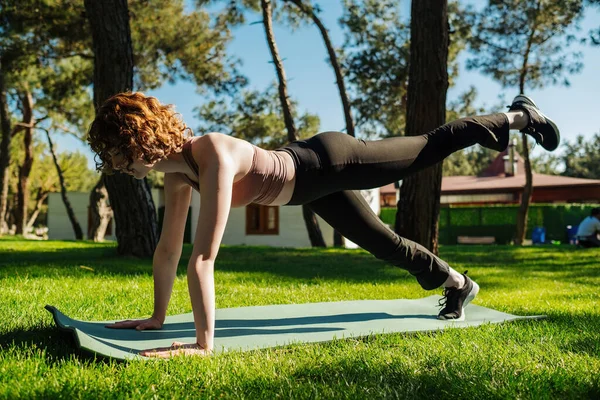 Sportif, genç ve güzel bir kadın yoga yapıyor. Egzersiz köpeği dengeliyor. Diz çökmüş, kol ve bacak uzatılıyor. Açık hava sporları kavramları.