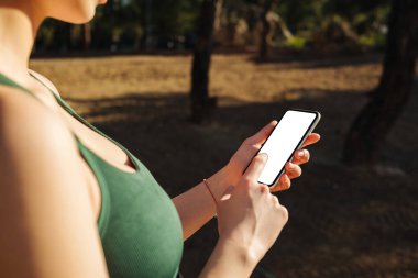 Genç sportif bir kadın cep telefonuyla parmak izi taraması yapıyor. Beyaz bir ekran, sosyal medya uygulaması ya da fitness uygulaması için boş bir ekran. Mobil uygulama teknolojisi konsepti, omuz üstü yakın çekim görünümü.