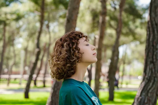 Yeşil tişörtlü kızıl saçlı bir kadın ormanda ve dışarıda dikiliyor. Stresten uzak, düşünceli anın tadını çıkarmak yoga egzersizleri yapmak, kapalı gözler meditasyon yapmak, nefes almak..
