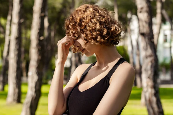 美丽的红头发女人穿着黑色运动胸罩站在城市公园 在户外揉揉鼻子和眼睛 感觉疲劳和头痛 压力和挫折的概念 按摩鼻桥 — 图库照片