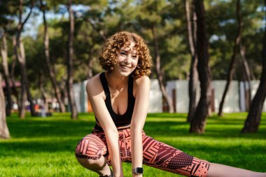 Şehir parkında sportif kıyafetler giyen sevimli bir kadın, açık havada bacak kaslarını esnetiyor, skandasana pozunda yan hamleler yapıyor. Sağlıklı yaşam tarzı kavramı.