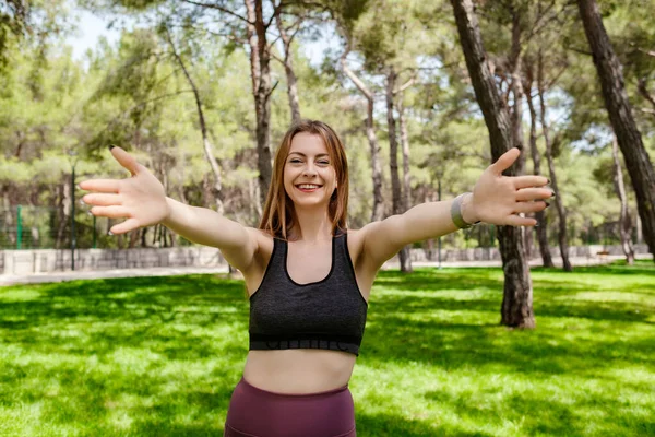 Cheerful brunette woman wearing sportive clothes on city park, outdoors looking at the camera smiling with open arms for hug. cheerful expression embracing happiness. Come here to us calling.