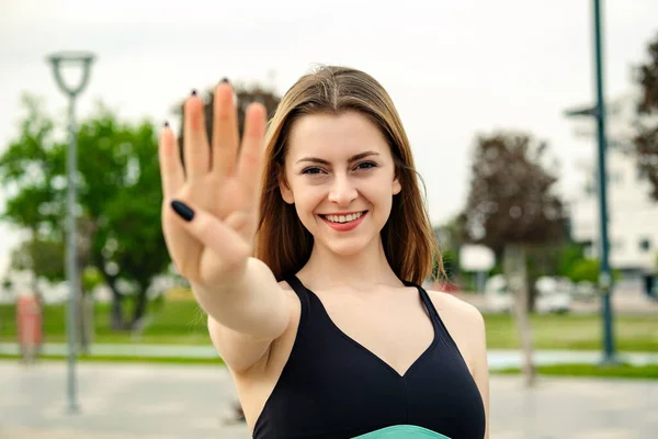 市内公園に立って黒のスポーツブラジャーを身に着けている幸せなブルネットの女性は 自信と幸せ笑顔ながら 指の数4を示して指摘しています 彼女の顔に焦点を当て — ストック写真
