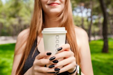 Siyah spor sutyen giyen esmer bir kadın şehir parkında duruyor, açık havada göğsünün önünde kahve fincanı tutuyor ve gözleri kapalı. Kahve sever ve açık hava sporu kavramları.