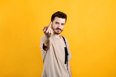 Handsome young man wearing casual clothes posing isolated over yellow background showing middle finger doing fuck you bad expression.