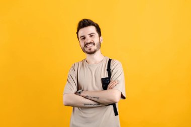 Beyaz tişört giyen beyaz bir adam sarı arka planda izole edilmiş poz veriyor. Kameraya bakarken kolları çapraz gülümsüyor. Pozitif kişi.