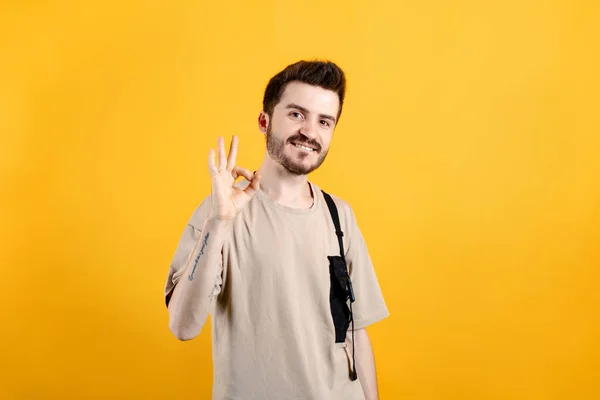 Happy casual man wearing t-shirt posing isolated over yellow background showing an ok sign with fingers. Symbol of good, top, best, champion, satisfied, and proud.