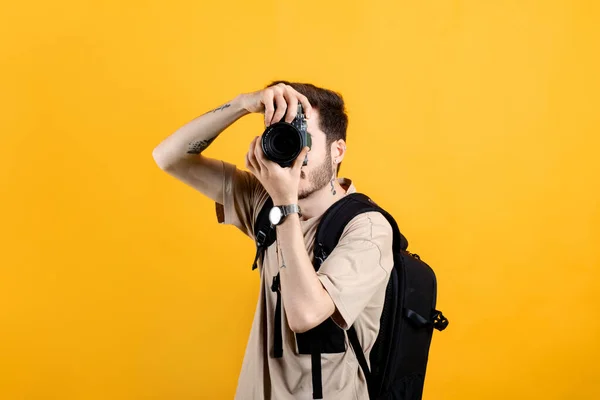 身穿T恤的白人年轻人在黄色背景上摆出孤立的姿势 用飞镖相机拍照 摄影师用照相机盖住他的脸 — 图库照片