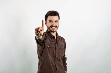 Beyaz arka planda yalnız poz veren mutlu genç adam gülümserken parmaklarıyla bir numarayı gösteriyor ve işaret ediyor..