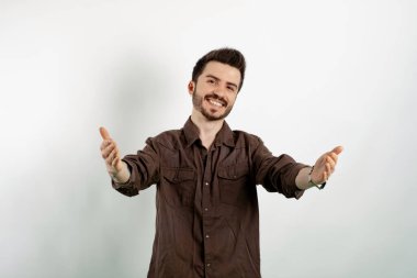 Kahverengi gömlekli neşeli beyaz adam beyaz arka planda yalnız poz veriyor. Sarılmak için kollarını açmış gülümsüyor. Mutluluğu kucaklayan neşeli bir ifade..
