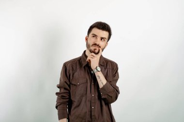 Beyaz arka planda yalnız poz veren beyaz tişörtlü beyaz bir adam sağ üst köşeye bakıp dudağa dokunuyor ve düşünüyor. Çözüm bulmaya çalışıyorum..