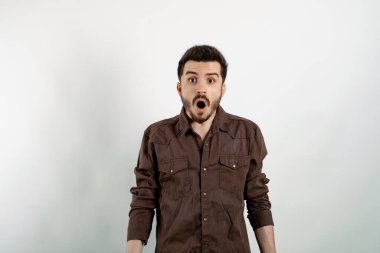 Beyaz arka planda izole edilmiş gündelik giysiler giyen yakışıklı genç adam yanlışlıkla ağzını kapatırken şok oldu. Gizli konsept. Kameraya bakıyorum..