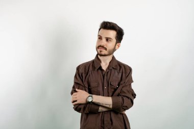 Beyaz arka planda soyutlanmış gibi duran beyaz giysili yakışıklı beyaz adam kollarını kavuşturuyor ve gülümseyerek başka tarafa bakıyor..