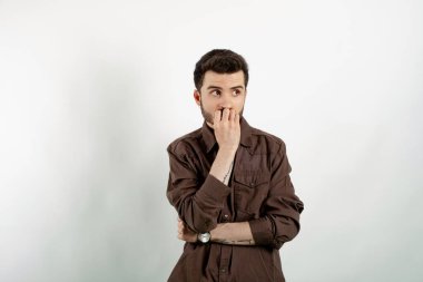 Beyaz arka planda soyutlanmış gibi görünen beyaz giysili yakışıklı beyaz bir adam çeneye dokunuyor ve başka tarafa bakıyor. Arama çözümü ya da karar verme kavramı.