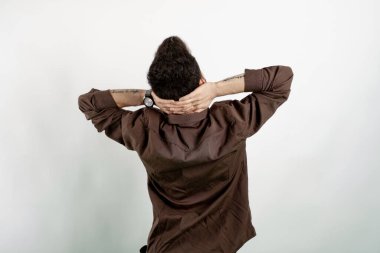 Yakışıklı, sıradan kıyafetler giyen, beyaz arka planda soyutlanmış, esnemiş, kolları ve elleri başının arkasında duran genç bir adam..