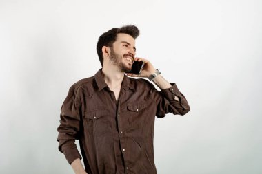 Yakışıklı, sıradan kıyafetler giyen, beyaz arka planda yalnız poz veren, akıllı telefonlardan konuşan ve gülümseyen bir genç. Telefon görüşmeleri sırasında iyi haberler alınıyor.