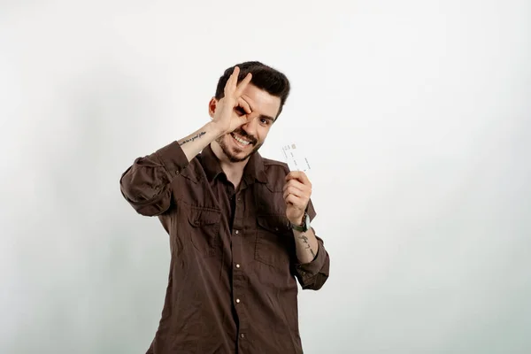 Happy young man wearing shirt posing isolated over white background holding credit bank card and showing okay gesture looking at the camera.