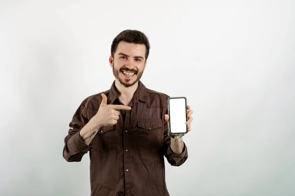 Beyaz arka planda izole edilmiş, kameraya gösterilen ve cihazı işaret eden günlük kıyafetler giyen yakışıklı beyaz bir adam. Model için boş alanı olan Gadget. Beyaz boş ekran.