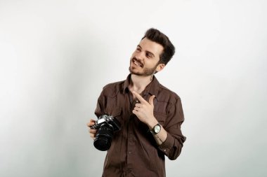 Kahverengi gömlekli neşeli beyaz adam beyaz arka planda yalnız poz veriyor gülümseyen adam işaret parmağıyla sol köşeyi gösteriyor ve bakıyor..