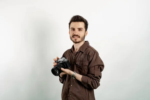 Happy young man wearing shirt posing isolated over white background posing with his dslr camera and his professional photographic equipment.