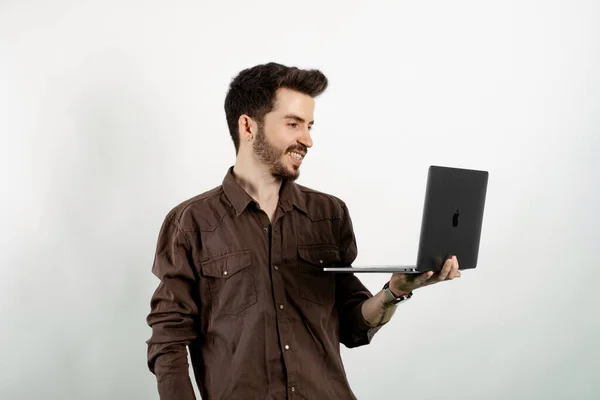 Happy young man wearing shirt posing isolated over white background standing and using laptop pc computer smiling with a happy and cool smile on face. Showing teeth.