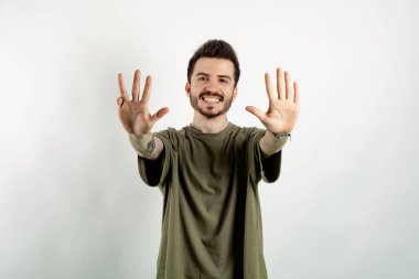 Yeşil tişört giyen, kendine güvenen genç bir adam beyaz arka planda izole edilmiş bir şekilde poz veriyor ve dokuz numarayı işaret ederek gülümsüyor..