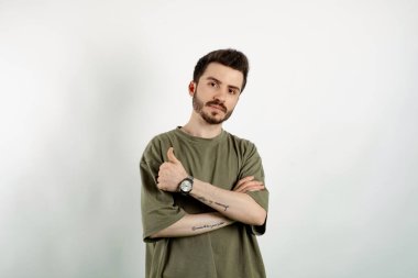 Yakışıklı, sıradan kıyafetler giyen, beyaz arka planda soyutlanmış bir şekilde poz veren, kameraya bakan, dostça gülümseyen, başparmak hareketi yapan genç bir adam.