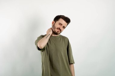 Beyaz arka planda izole edilmiş haki tişört giyen yakışıklı beyaz adam fiziksel rahatsızlık hissediyor sağlıksız yorgunluk gözlerini boynu ağrıdığı için kapattı. Omuz ağrısı konsepti.