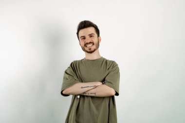 Kendinden emin gülümseyen genç bir adam beyaz arka planda izole bir şekilde poz veriyor ve kollarını kavuşturup kameraya bakıyor. Pozitif kişi.