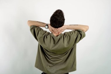 Yakışıklı, sıradan kıyafetler giyen, beyaz arka planda soyutlanmış, esnemiş, kolları ve elleri başının arkasında duran genç bir adam..