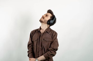 Beyaz arka plandaki kablosuz kulaklıklar üzerinden izole edilmiş tişört giyen, meditasyon yapan, sesli rehber kullanan beyaz bir genç. Kulaklığa dokunuyorum..