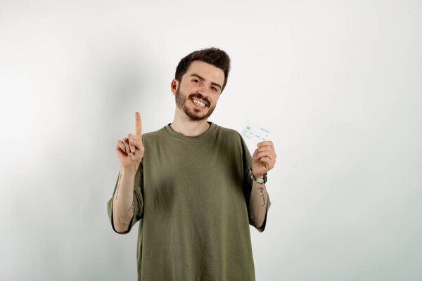 Счастливый случайный человек в футболке позирует изолированно на белом фоне держа кредитную карту и указывая рукой и пальцем в сторону.