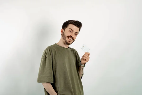 Happy casual man wearing t-shirt posing isolated over white background holding credit card and smiling with a confident smile showing teeth.