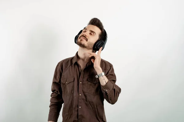 Caucasian young man wearing shirt posing isolated over white background wireless headphones meditating listening audio guide. Touching to headphone.