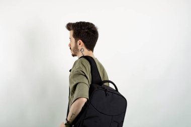 Haki tişört giyen genç bir adam, beyaz arka plan öğrencisinin üzerinde, boynunda kulaklık olan bir sırt çantasıyla poz veriyor. Arka plan fotoğrafı.