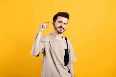 Beyaz tişört giyen, sarı arka planda izole edilmiş beyaz bir adam parmaklarıyla ölçü alırken kameraya bakıyor. Acıyarak küçük boy uzunluğu gösteriyor.